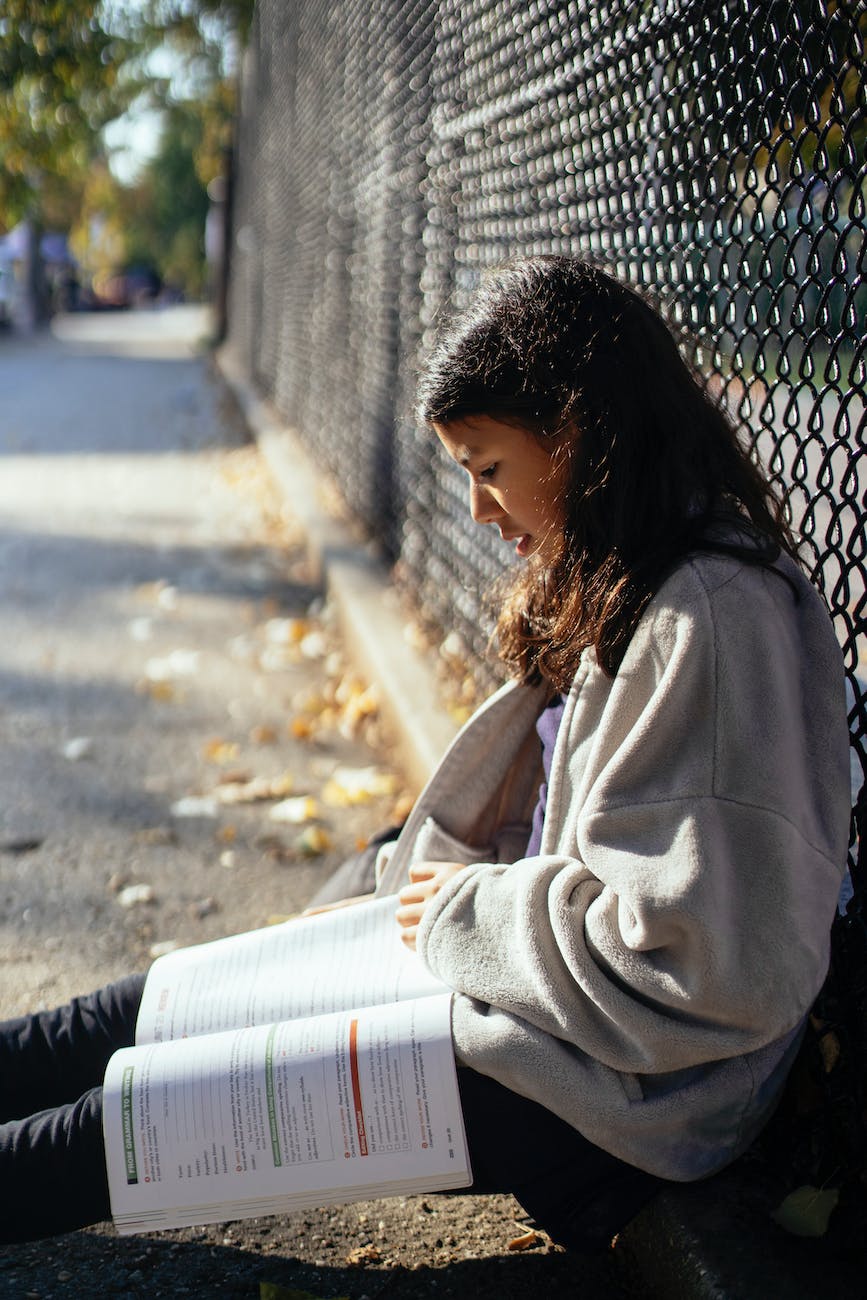 teenage girl reading textbook on street